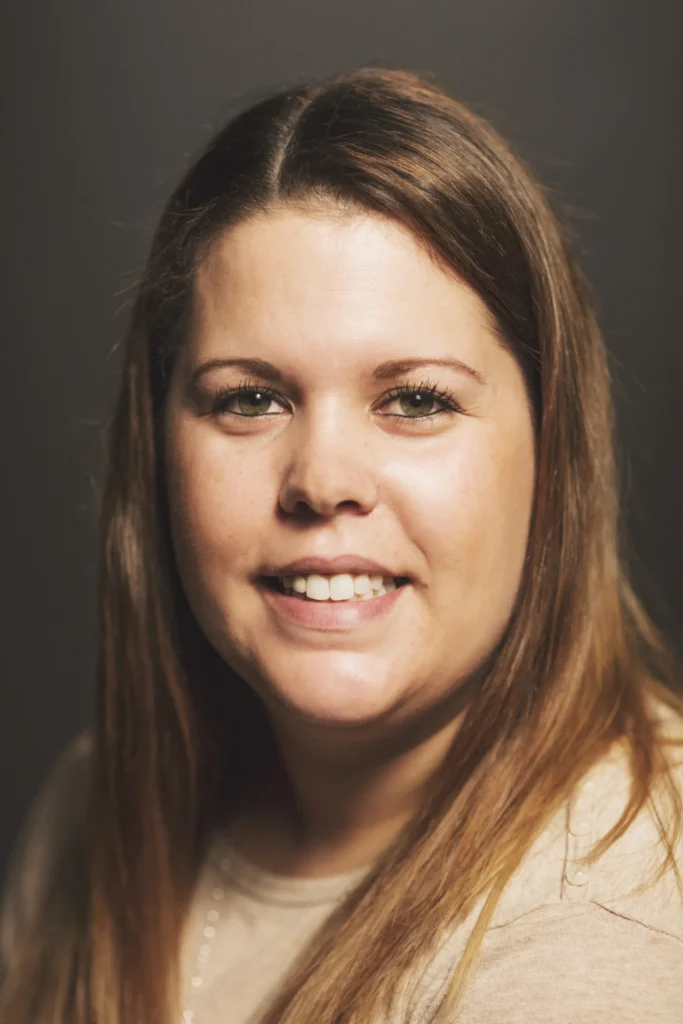 A person with long brown hair against a gray background.